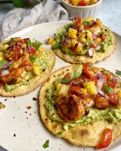 three tortillas topped with shrimp, avocado and salsa on a white plate