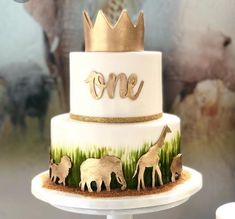 a three tiered cake decorated with animals and the word one on top is gold