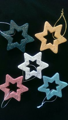 four wooden stars are hanging from strings on a black background, one is white and the other is pink