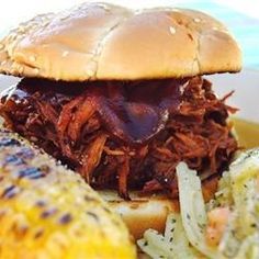 a pulled pork sandwich with coleslaw and corn on the cob