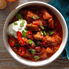 a white bowl filled with meat, tomatoes and sour cream on top of a wooden table