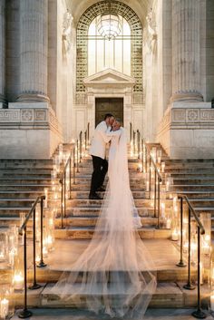 a bride and groom kissing on the steps of a church with candles in front of them