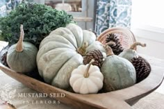 a wooden bowl filled with white pumpkins and pine cones on top of a table