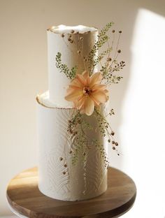 a three tiered wedding cake with flowers on top is sitting on a wooden plate