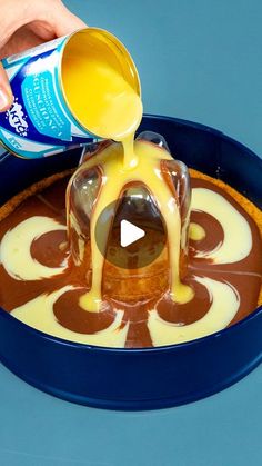 a person pouring caramel sauce on top of a cake in a blue pan with white icing