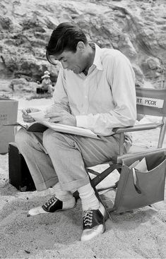 a man sitting in a chair on the beach with his feet up and reading a book