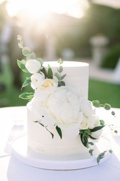 a white wedding cake with flowers and greenery on the top is sitting on a table