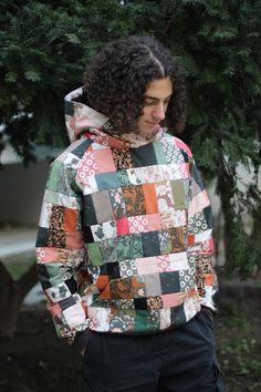 a man standing in front of a tree wearing a jacket with patchwork on it