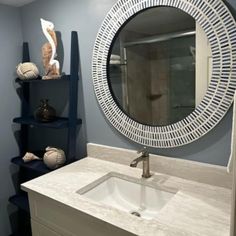 a white sink sitting under a round mirror in a bathroom next to a book shelf