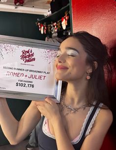 a woman is holding up a sign for an upcoming show in front of her face