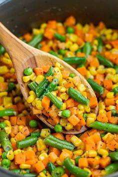 a wooden spoon is full of vegetables and corn in a pot with a wooden spoon