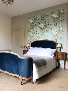 a bed with blue upholstered headboard and foot board in a room with floral wallpaper