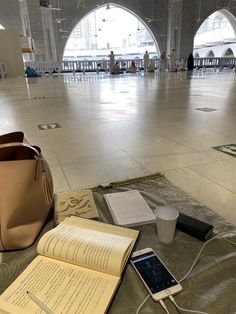 an open book, cell phone and cup on the floor in a large room with arches