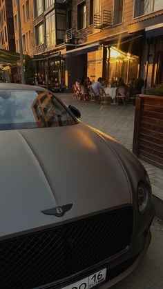 a car parked in front of a building with people sitting at tables on the sidewalk