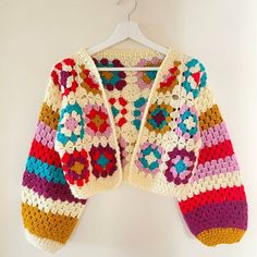 a colorful crocheted sweater hanging on a white wall next to a hanger