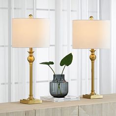 two lamps on a table with a plant in a vase