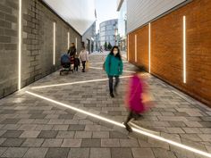 several people walking down a brick walkway with lights on the side of it and one woman in a pink coat