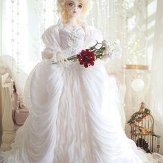 a doll is dressed in white and holding flowers