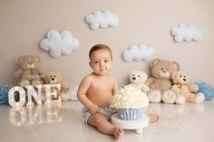 a baby sitting on the floor with a cake in front of him and teddy bears