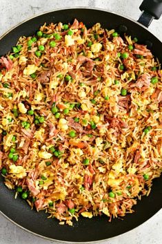 a skillet filled with rice and peas on top of a white countertop next to a spatula