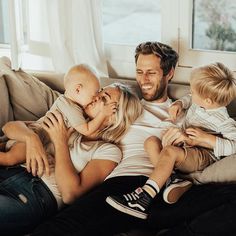 a man and woman sitting on a couch with two small children, one is kissing the other's cheek