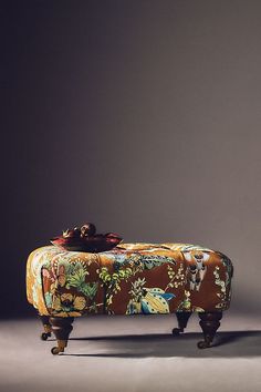 an upholstered bench with floral fabric on the legs and foot rests against a gray background