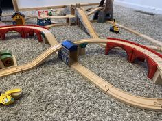 a child's toy train set with wooden tracks and cars on carpeted floor