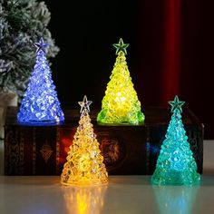 three small christmas trees sitting on top of a table next to a tree with lights