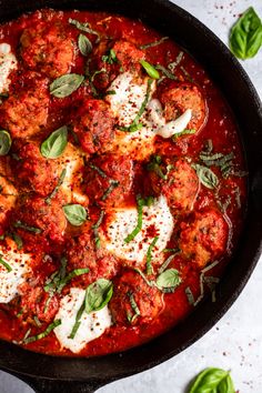 a skillet filled with meatballs covered in marinara sauce and fresh basil leaves