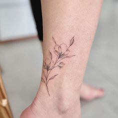 a small flower tattoo on the ankle is shown in black and grey ink, with leaves