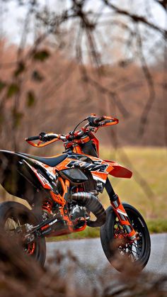 an orange and black dirt bike is in the air on a road near some trees