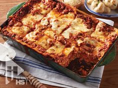 a casserole dish with meat and cheese in it on a table next to garlic bread