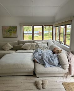 a person laying on top of a white couch in a living room next to two windows