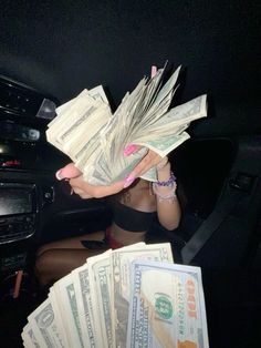 a woman sitting in the back seat of a car holding up stacks of money to her face