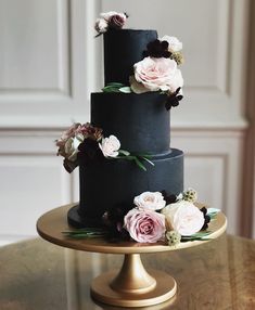 a three tiered black wedding cake with pink and white flowers