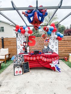 an outdoor birthday party with balloons and spiderman decorations on the table in front of it