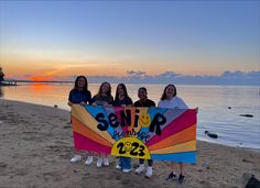 four girls standing on the beach holding a sign that says semp and smiles at sunset