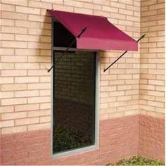 a red awning on the side of a brick building with grass growing in it