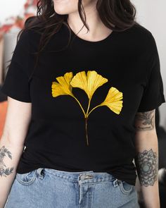 T-shirt featuring a botanical illustration of a fall Gingko leaf. Fall in love with our autumn leaves shirt you won't find anywhere else. Printed on a black cotton t-shirt, made from durable lightweight cotton. Unisex fit - boxy and long. How it's made: * All prints are original watercolor designs hand-painted by a botanical artist. * Ethically made 100% cotton t-shirts that are made to last. * T-shirts are printed and shipped by my printing partner in the US, Canada, or Europe. * By buying from this shop you are directly supporting a woman-owned small business, created out of love for plants to educate, inspire and keep us connected to the natural world. About the artist: This Shop is an extension of my botanical illustration studio, where I create hand-painted watercolor art for internat Casual Fall Shirt With Plant Print, Fall Yellow Printed T-shirt, Yellow Printed T-shirt For Fall, Casual T-shirt With Plants Print For Fall, Casual Plants Print T-shirt For Fall, Casual Fall T-shirt With Plant Print, Fall Crew Neck T-shirt With Plants Print, Fall Short Sleeve Shirt With Plants Print, Botanical Crew Neck T-shirt For Fall