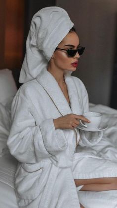 a woman in a bathrobe sitting on a bed with a cup and saucer