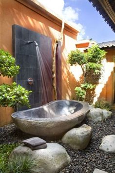 a bath tub sitting in the middle of a garden next to a tree and rocks