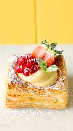 a pastry topped with berries and powdered sugar on a white tablecloth next to a yellow wall