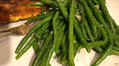 green beans and chicken on a white plate with a fork next to the side dish