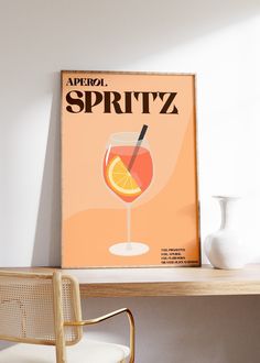 a poster with an orange drink in it on top of a wooden table next to a white vase