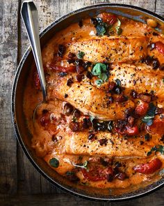 a pan filled with chicken, tomatoes and olives on top of a wooden table