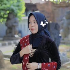 a woman wearing a hijab standing in front of a grave yard with a butterfly on her head