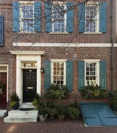 a brick house with green shutters and blue doors on the front door is surrounded by potted plants