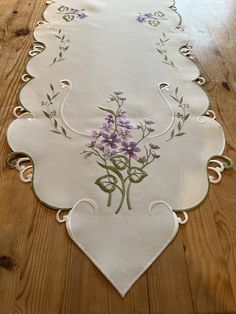 an embroidered table runner with purple flowers on white linen, sitting on a wooden floor