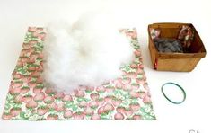 a cotton swab next to a wooden box filled with white fluffy balls on top of a pink and green flowered table cloth