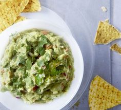 a white bowl filled with guacamole surrounded by tortilla chips